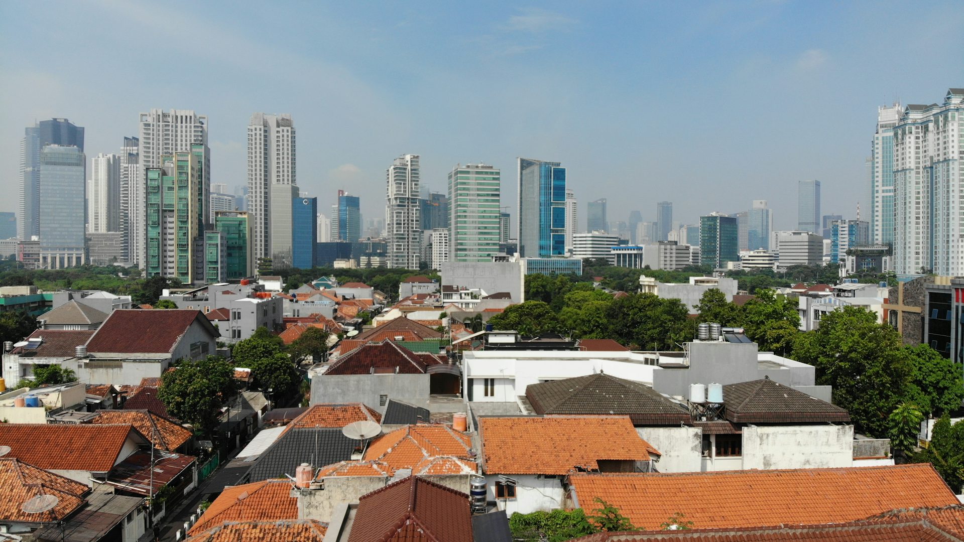 Atap rumah-rumah di perumahan dengan deretan gedung tinggi di kejauhan