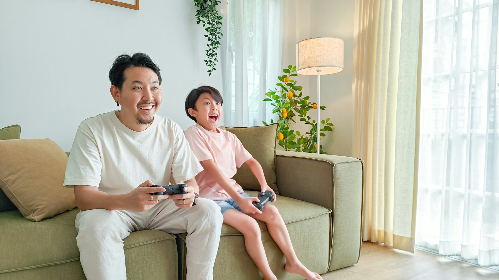 Father and son playing console games on the living room sofa