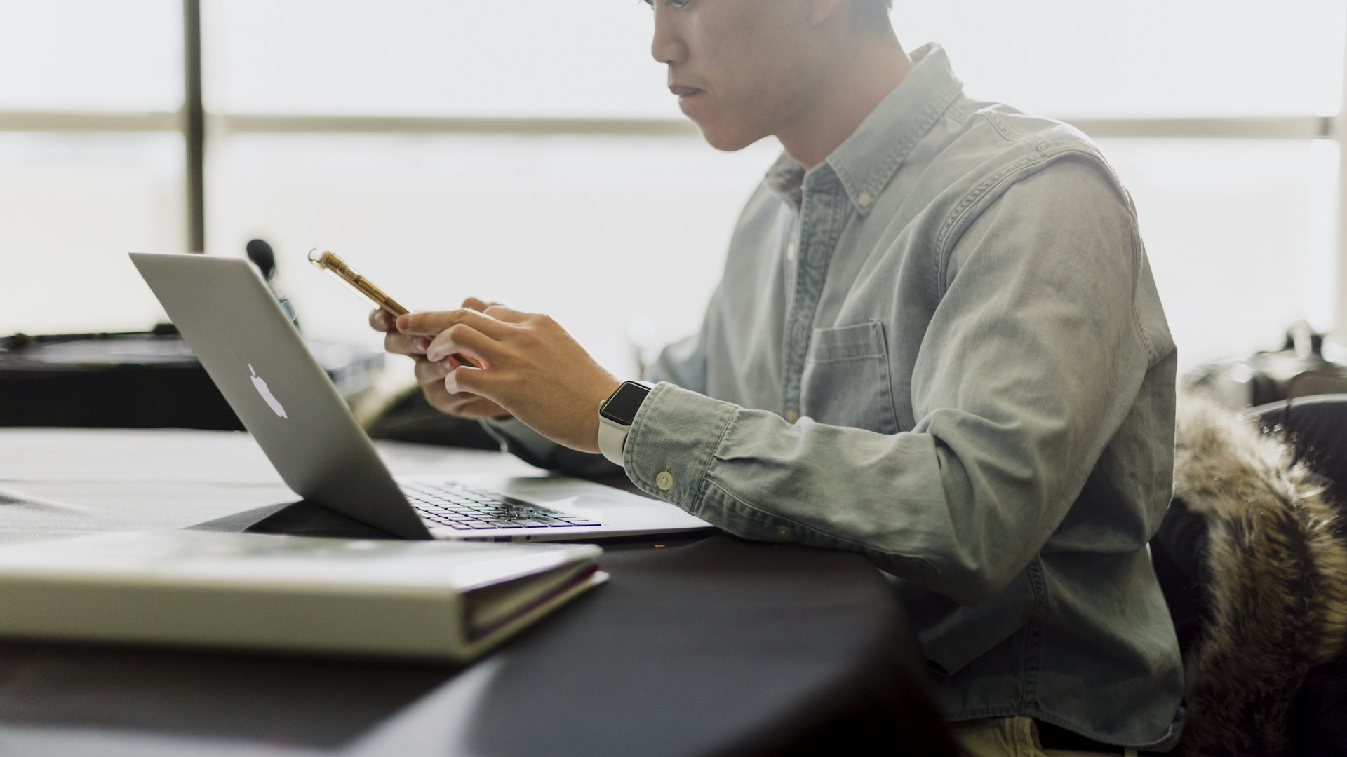 Karyawan bekerja dengan laptop sambil memegang ponsel di kantor