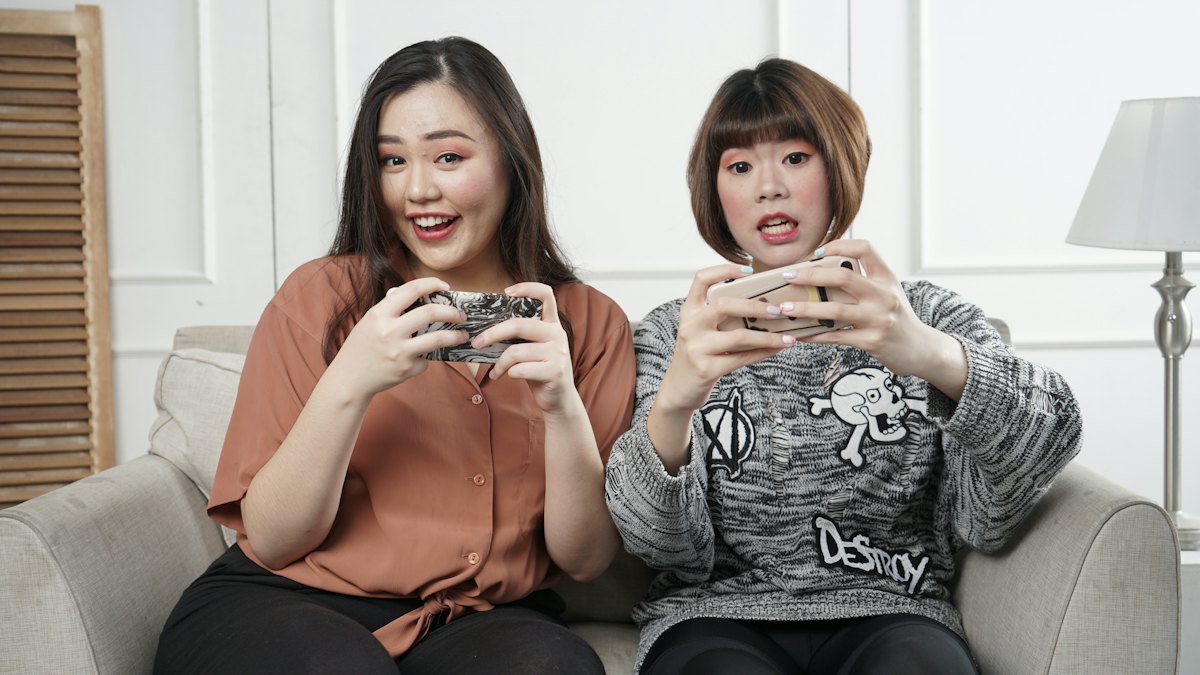 Two women playing games with controllers on a sofa