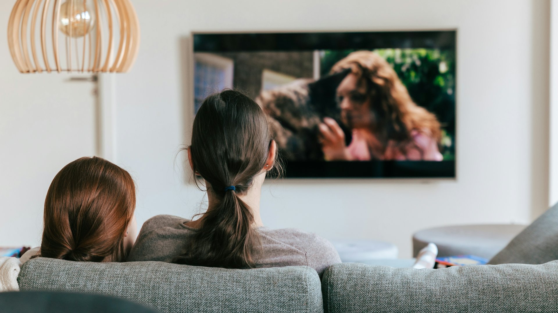 Dua orang duduk di sofa menonton televisi di ruang keluarga