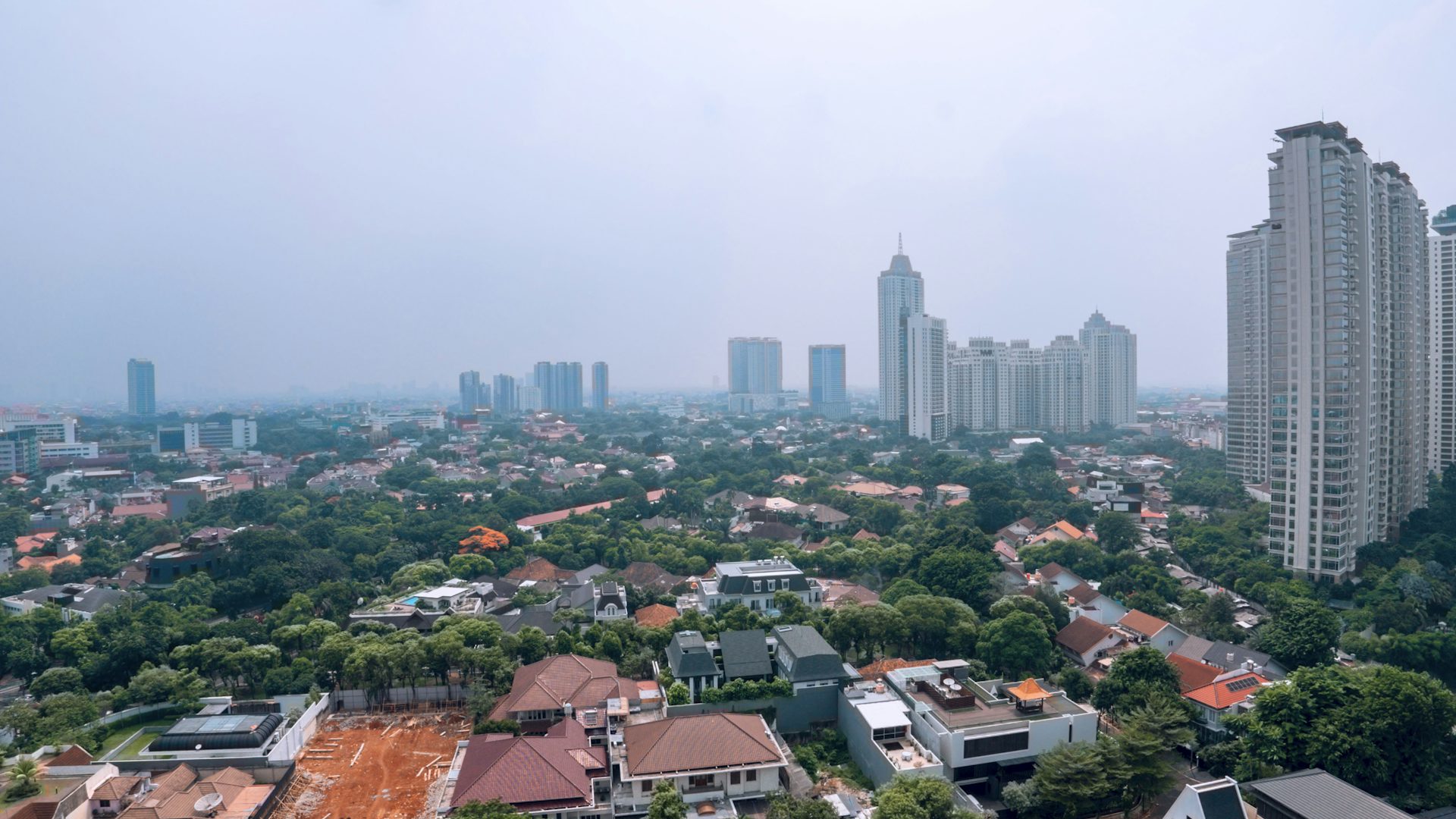 Pemandangan udara permukiman padat dengan gedung-gedung tinggi di kejauhan