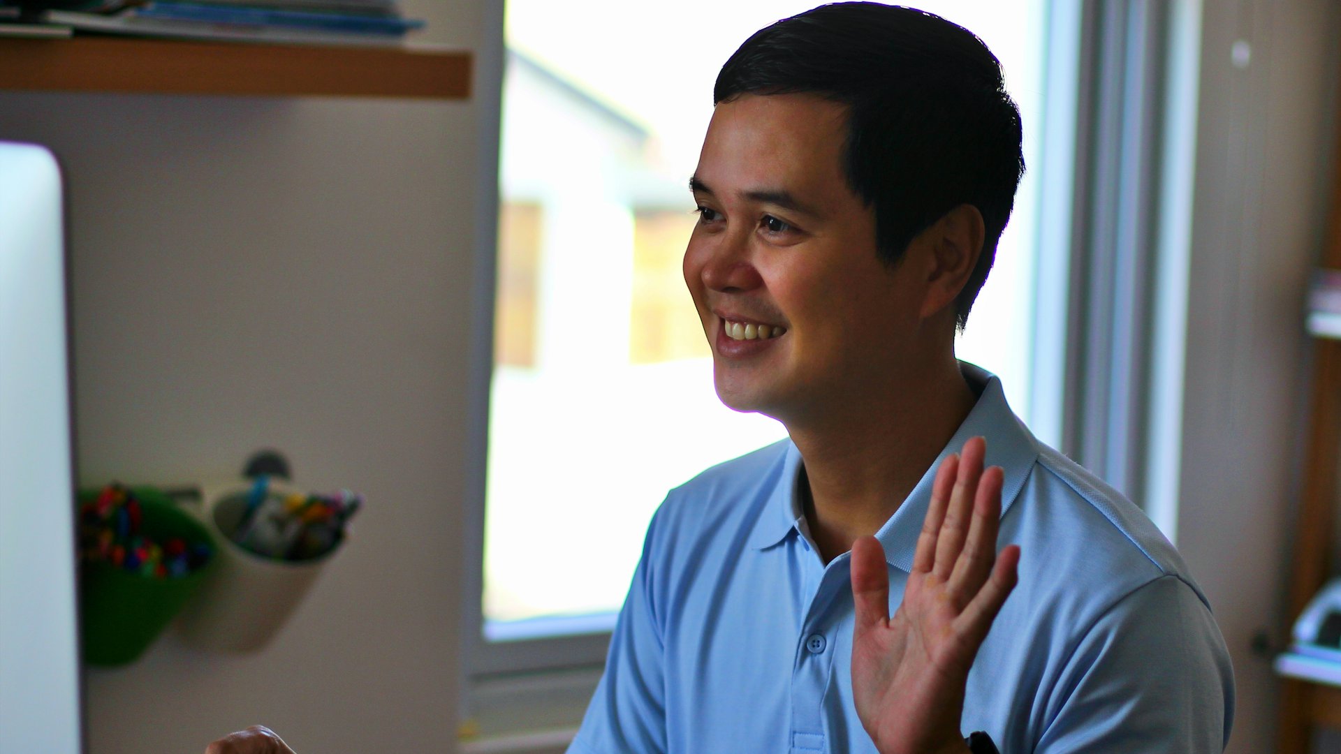 Smiling man waving during a video call on his laptop